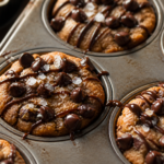 Brown butter tahini chocolate chip cookie cups in a muffin tin with glossy cocoa drizzle and flaky salt