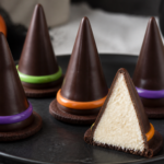 No-bake witch hat cheesecake cones on a Halloween dessert tray with dark chocolate coating and colorful bands