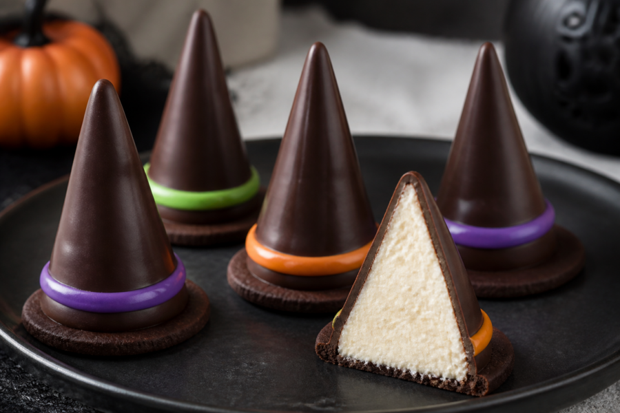 No-bake witch hat cheesecake cones on a Halloween dessert tray with dark chocolate coating and colorful bands