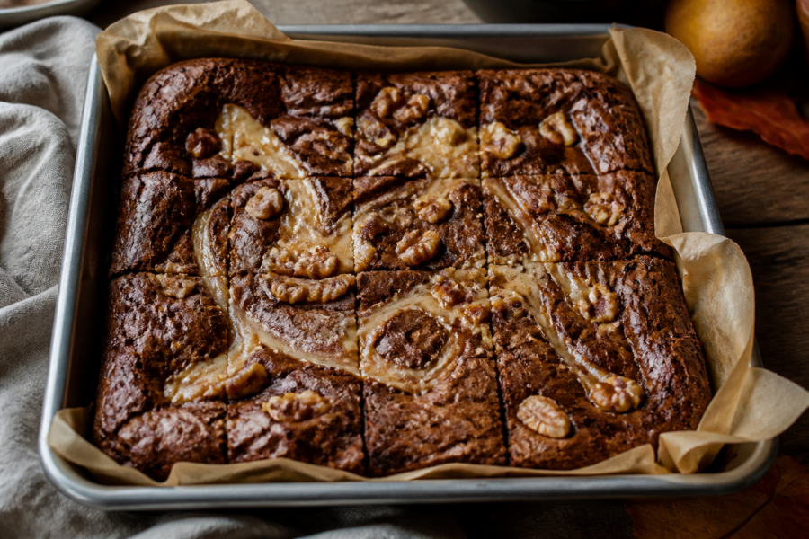 Finished brown butter pear caramel swirl brownies in a square pan with a glossy pear caramel swirl and toasted nut topping