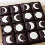 Finished 8x8 Halloween black cocoa moon phase brownies with vanilla glaze in a clean grid of white crescents