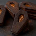 Black cocoa Halloween coffin linzer cookies with dulce de leche window cutouts stacked like sandwich cookies