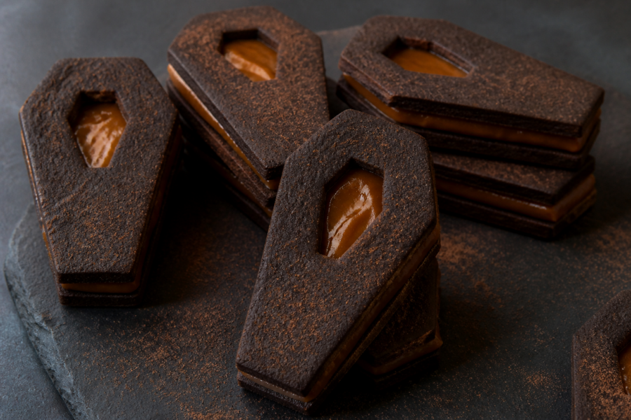 Black cocoa Halloween coffin linzer cookies with dulce de leche window cutouts stacked like sandwich cookies