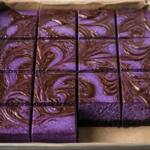 Black magic ube Oreo cheesecake bars with a glossy dark-chocolate swirl in a square pan