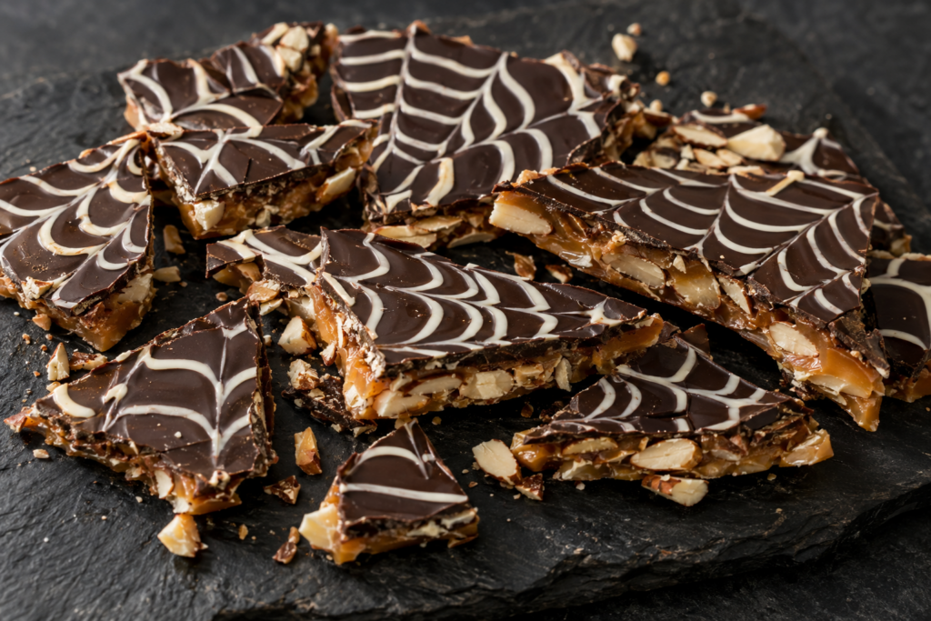 Finished Halloween spiderweb dark chocolate almond toffee in a 9×13 pan, sliced into pieces with a white chocolate spiderweb on top.