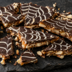 Finished Halloween spiderweb dark chocolate almond toffee in a 9×13 pan, sliced into pieces with a white chocolate spiderweb on top.