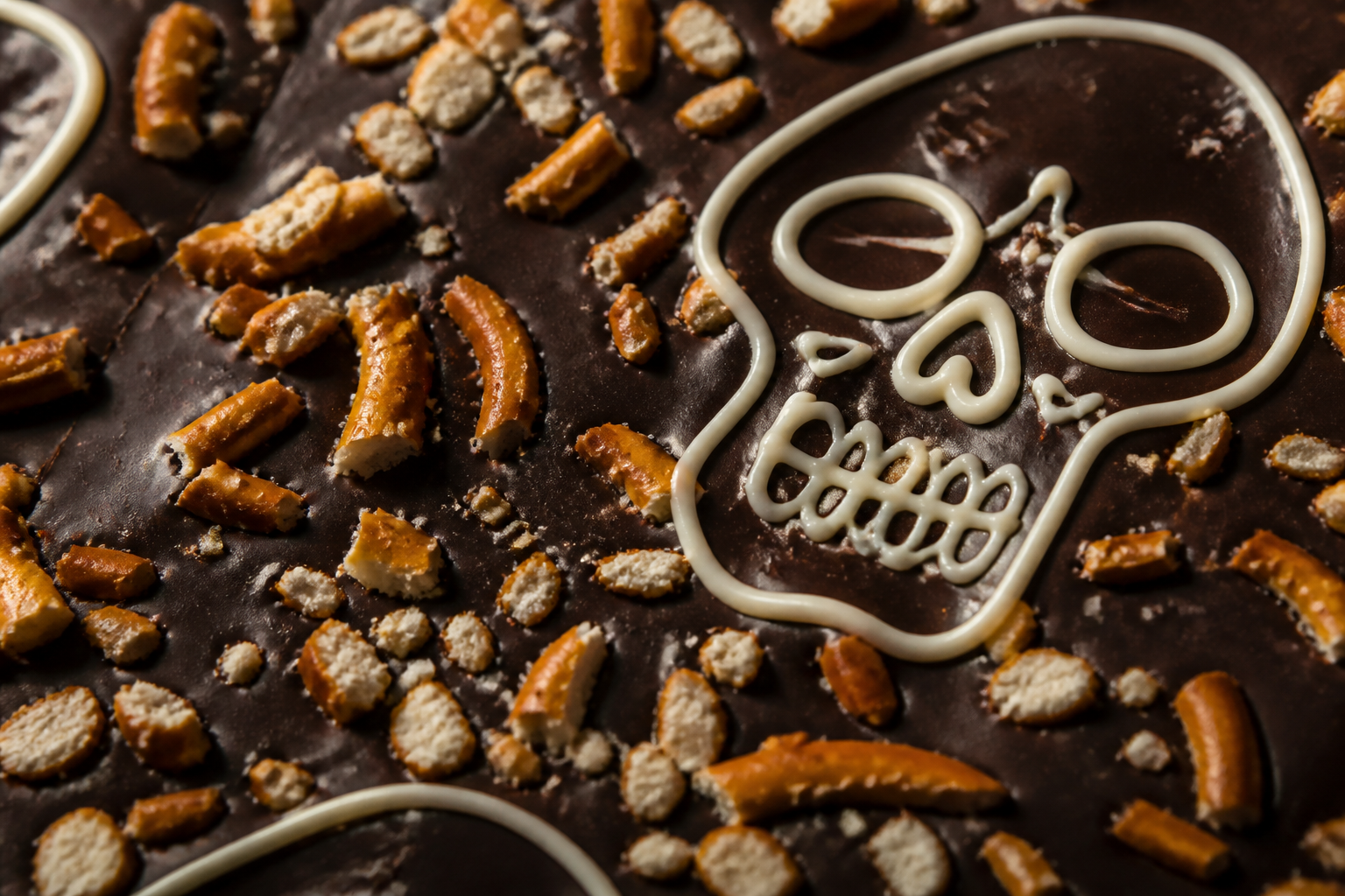 Close-up of crunchy pretzel bits and a crisp white chocolate skull outline on dark chocolate bark