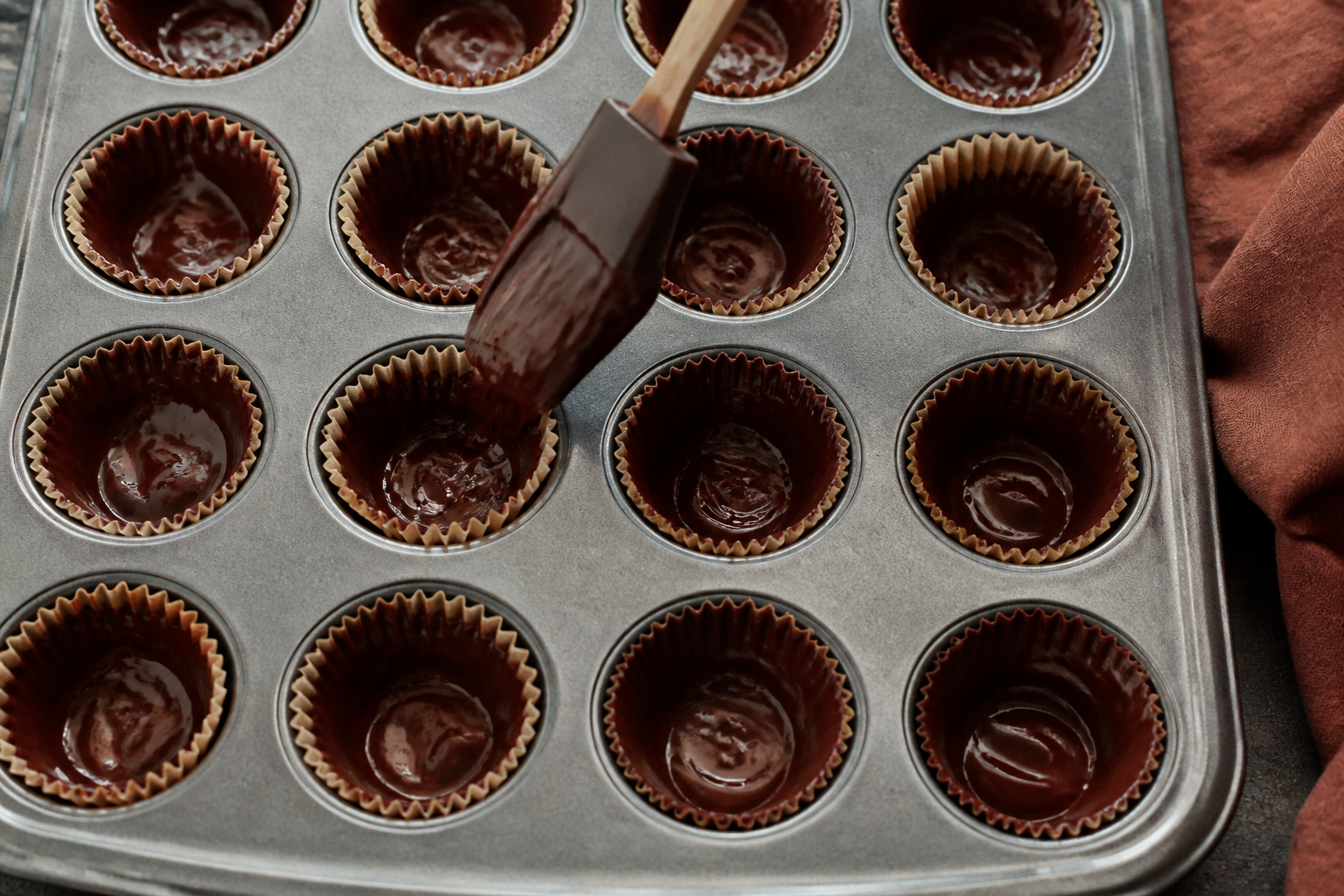 Close-up of dark chocolate being poured into mini muffin liners to create chocolate shells