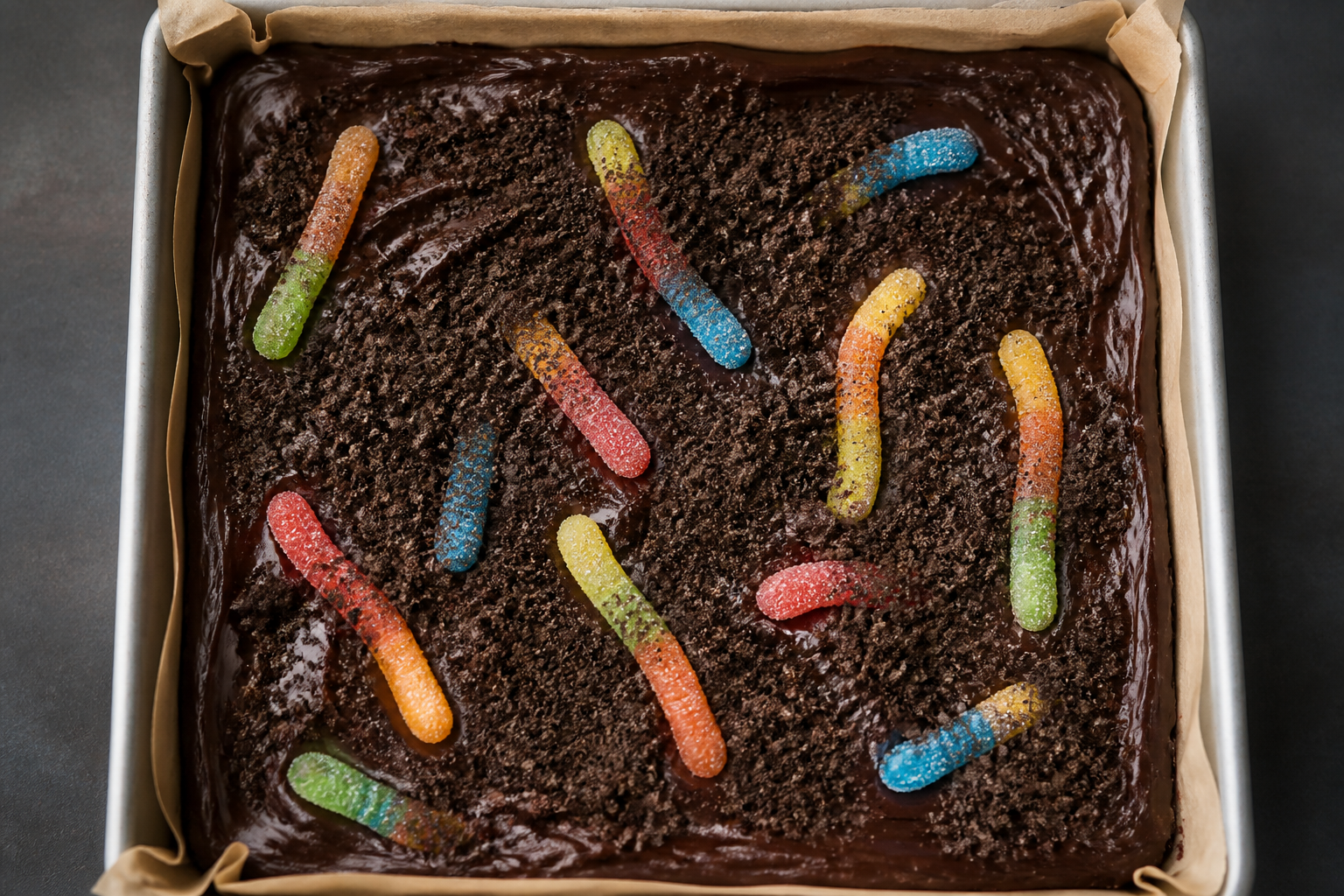 Cocoa cookie soil sprinkled on top with sour gummy worms pressed in before chilling