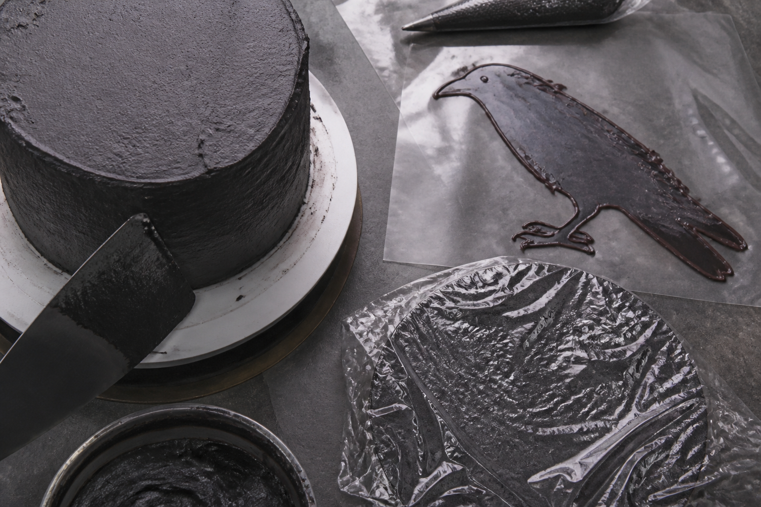 Stacking and crumb-coating the cake layers, with the raven acetate template nearby before chilling