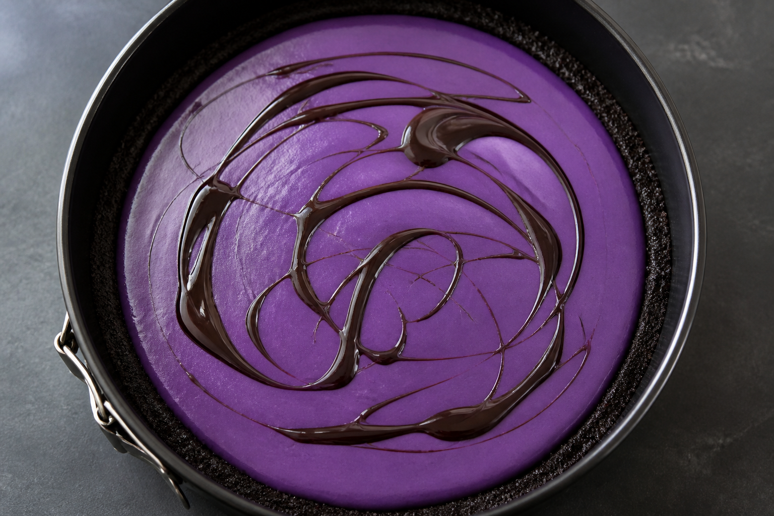 Pouring and smoothing the vivid purple ube cheesecake filling before adding the dark chocolate swirl
