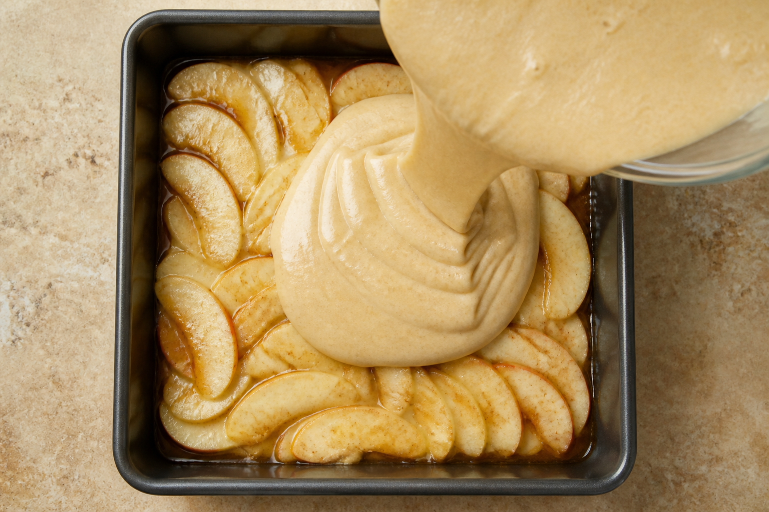 Top-down view of apples arranged and cake batter layered in the pan