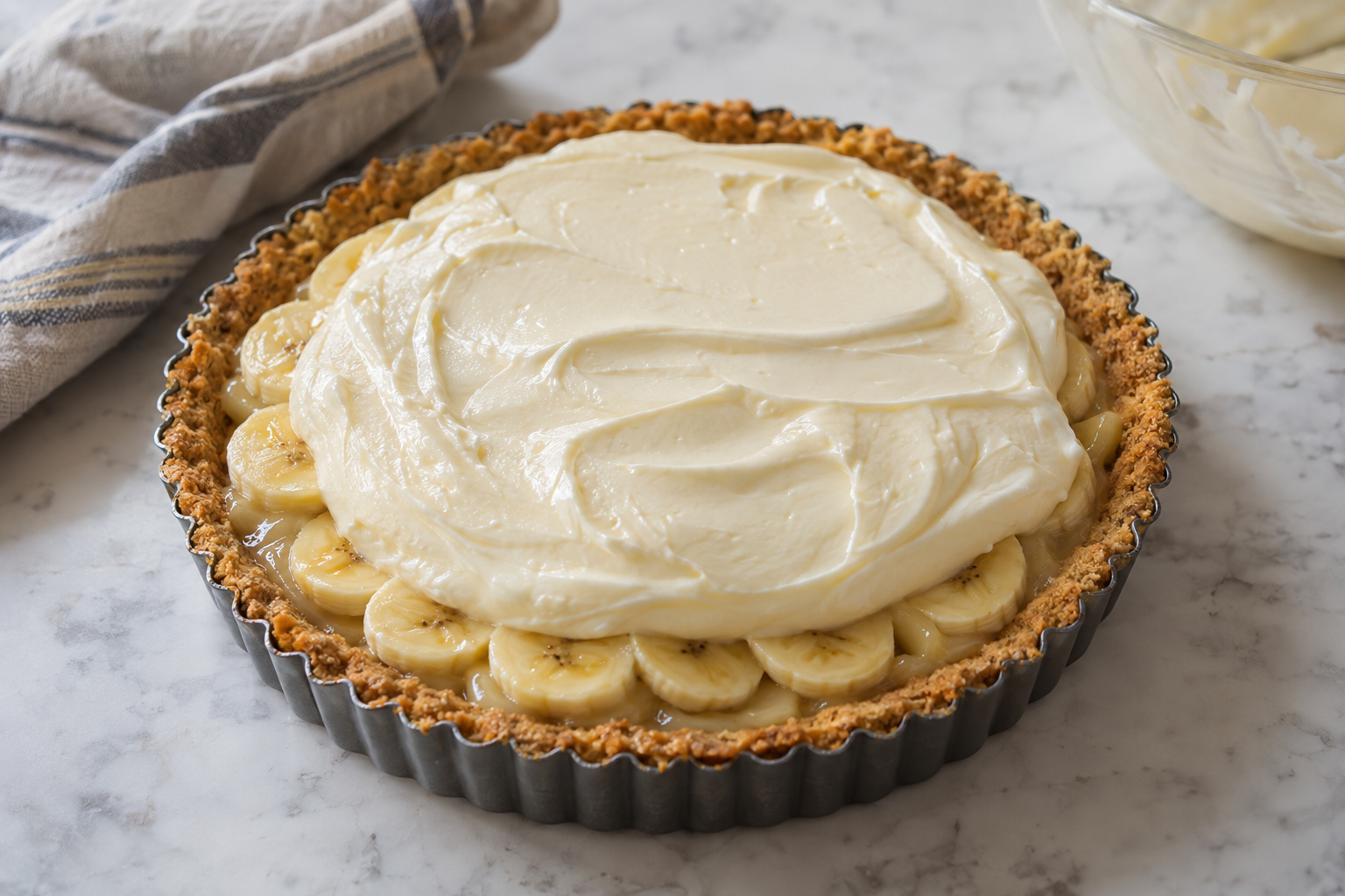 Assembled tart with banana layer and cheesecake filling ready to chill