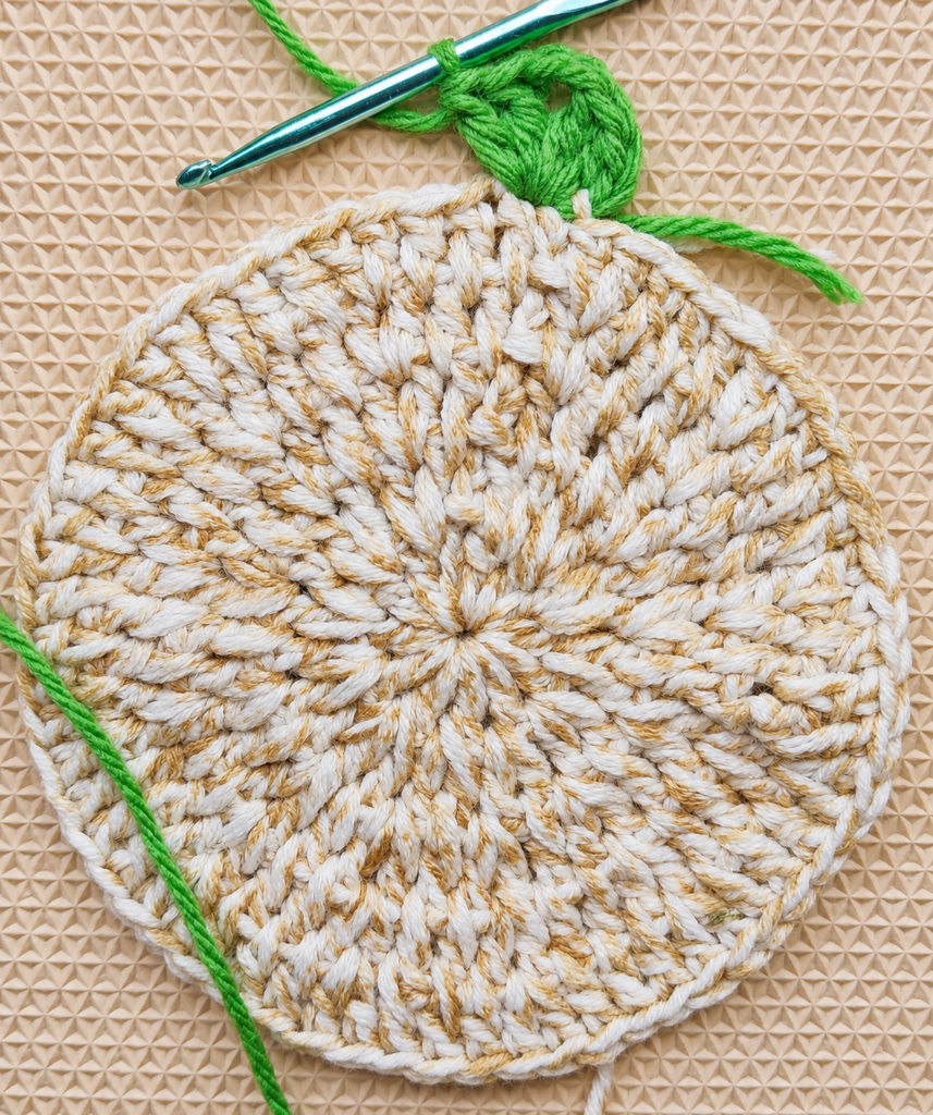 Second green V-stitch forming along the coaster edge.