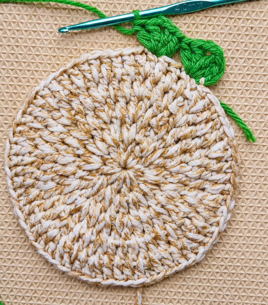 Several green V-stitch clusters completed around the cotton coaster.