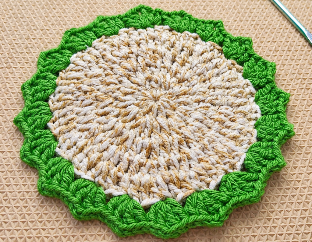 Finished sea grass crochet coaster lying flat with a green scalloped edge.