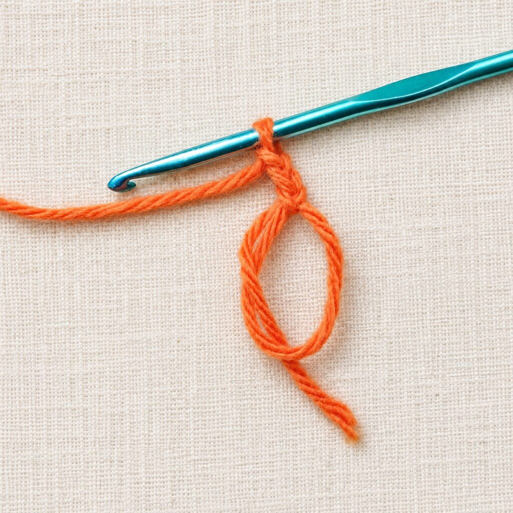Orange cotton yarn formed into a magic circle beneath a 4 mm crochet hook.