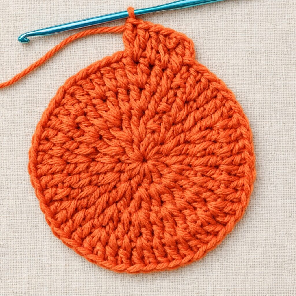 The crochet pumpkin potholder body growing evenly in joined rounds.