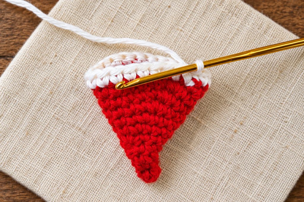 Nearly completed white crochet brim with the hook positioned at the joining stitch.