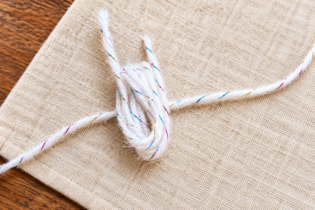 Long white strand tied firmly through the center of the looped pom-pom bundle.