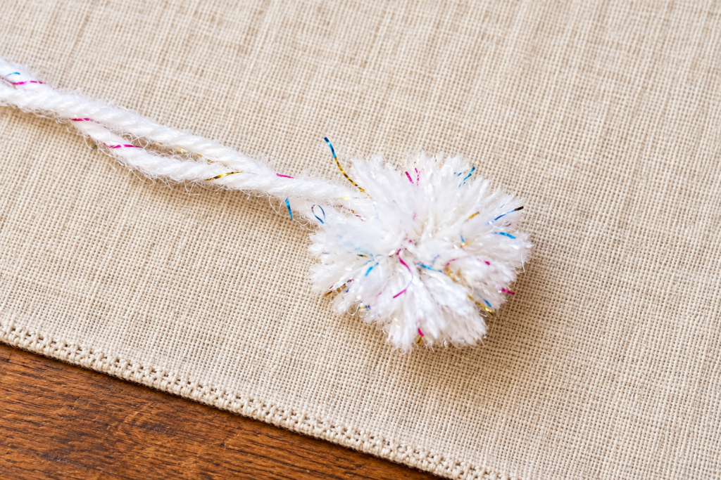 Finished fluffy white pom-pom with two long attachment strands left uncut.