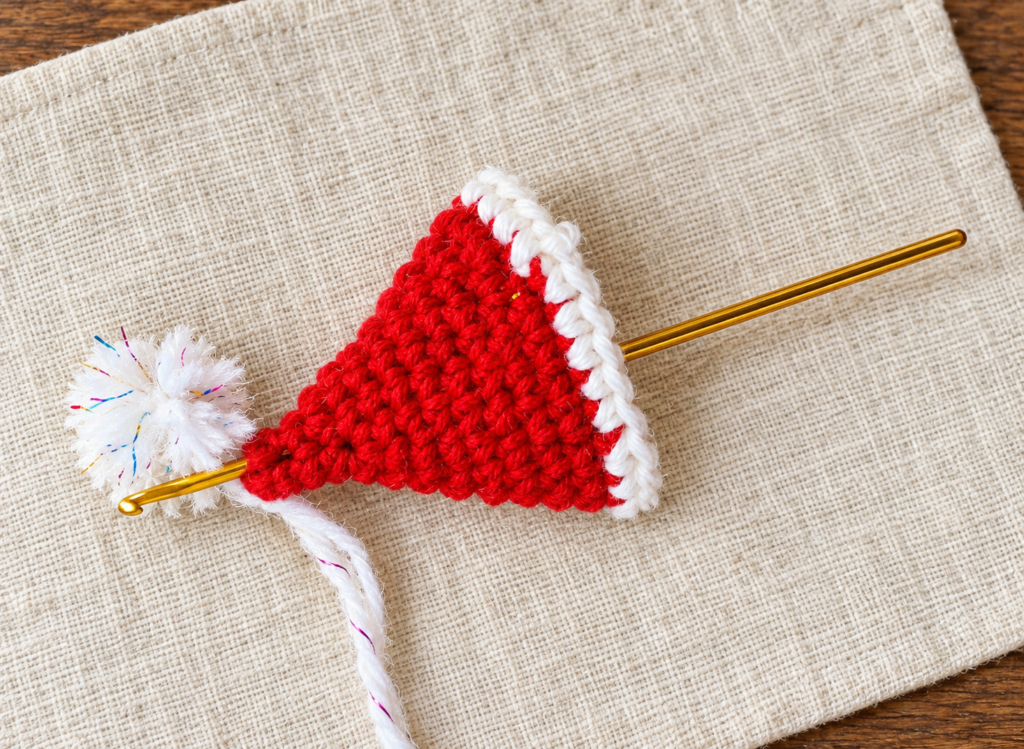 White pom-pom attachment strands being pulled through the pointed top of the red hat.