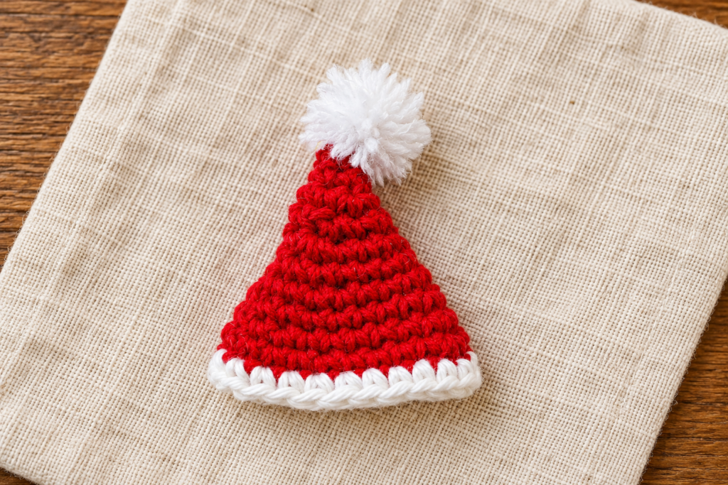 Completed crochet mini Santa hat with a white brim and securely attached pom-pom.