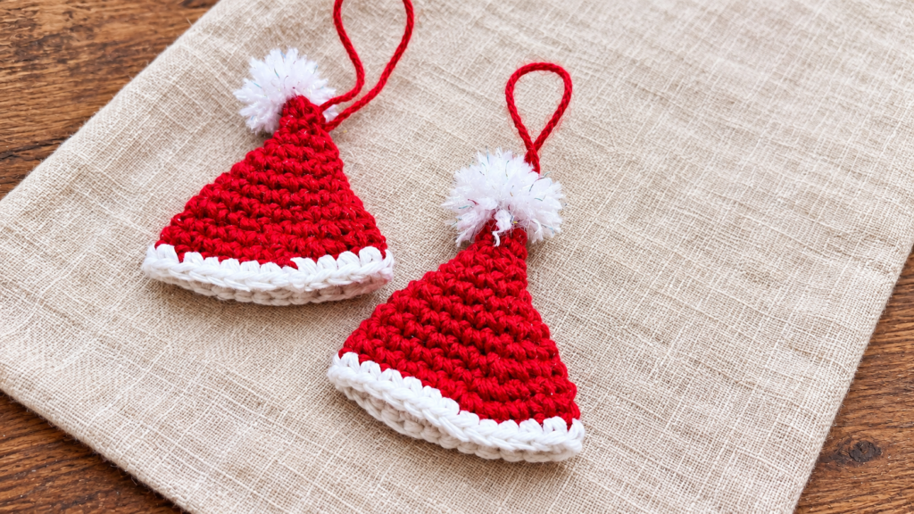 Two completed crochet mini Santa hat ornaments with red hanging loops.
